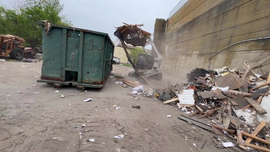 Skid steer loading demolition debris next to a roll-off dumpster